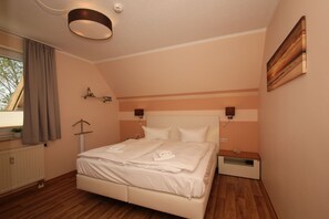 A bedroom with a bed, a nightstand, a wall-mounted lamp, a radiator, and a window with curtains. - Close to the beach, with a balcony; access to the pool and sauna - Strandhaus Mönchgut FeWo13 (Middelhagen)