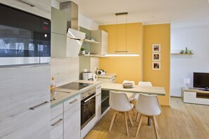 A modern kitchen with a built-in oven, a microwave, and a dining area with two white chairs. - Close to the beach with balcony, use of swimming pool and sauna - Strandhaus Mönchgut FeWo13 (Middelhagen)