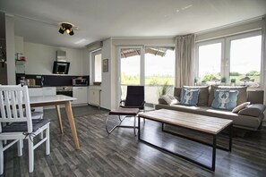 A modern living room with a sofa, coffee table, and dining area. - Close to the beach with balcony, use of swimming pool and sauna - Strandhaus Mönchgut FeWo11 (Middelhagen)