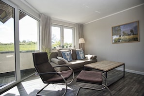 A modern living room with a sofa, two armchairs, a wooden coffee table, and a painting on the wall.