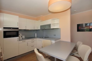 A compact kitchen with white cabinets, a built-in oven, a microwave, a sink, and a dining area with a table and chairs. - Close to the beach with a balcony; access to the pool and sauna - Strandhaus Mönchgut FeWo12 (Middelhagen)