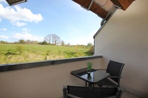 A balcony with a table and chairs, a small plant, and a view of a green field and trees. - Close to the beach with balcony, use of swimming pool and sauna - Strandhaus Mönchgut FeWo12 (Middelhagen)