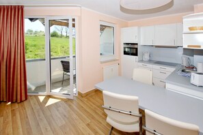 A modern kitchen with a large island, white cabinets, and a view to a balcony. - Close to the beach with balcony, use of swimming pool and sauna - Strandhaus Mönchgut FeWo12 (Middelhagen)