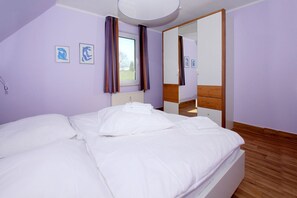 A bedroom with a bed, a window with curtains, a mirror, and a radiator. - Close to the beach with balcony, use of swimming pool and sauna - Strandhaus Mönchgut FeWo12 (Middelhagen)