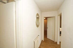 Un couloir étroit aux murs blancs, doté d’un plancher en bois et d’un radiateur.