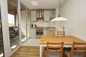 Une cuisine compacte avec un coin repas, comprenant une table et des chaises en bois, un four encastré et un petit réfrigérateur.
