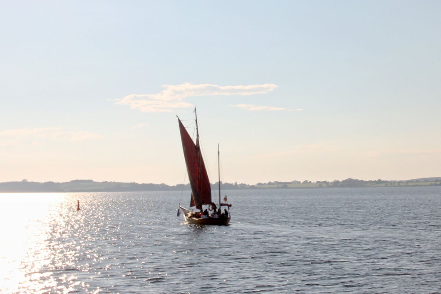 Ein Segelboot mit rotem Segel auf ruhigem Wasser.