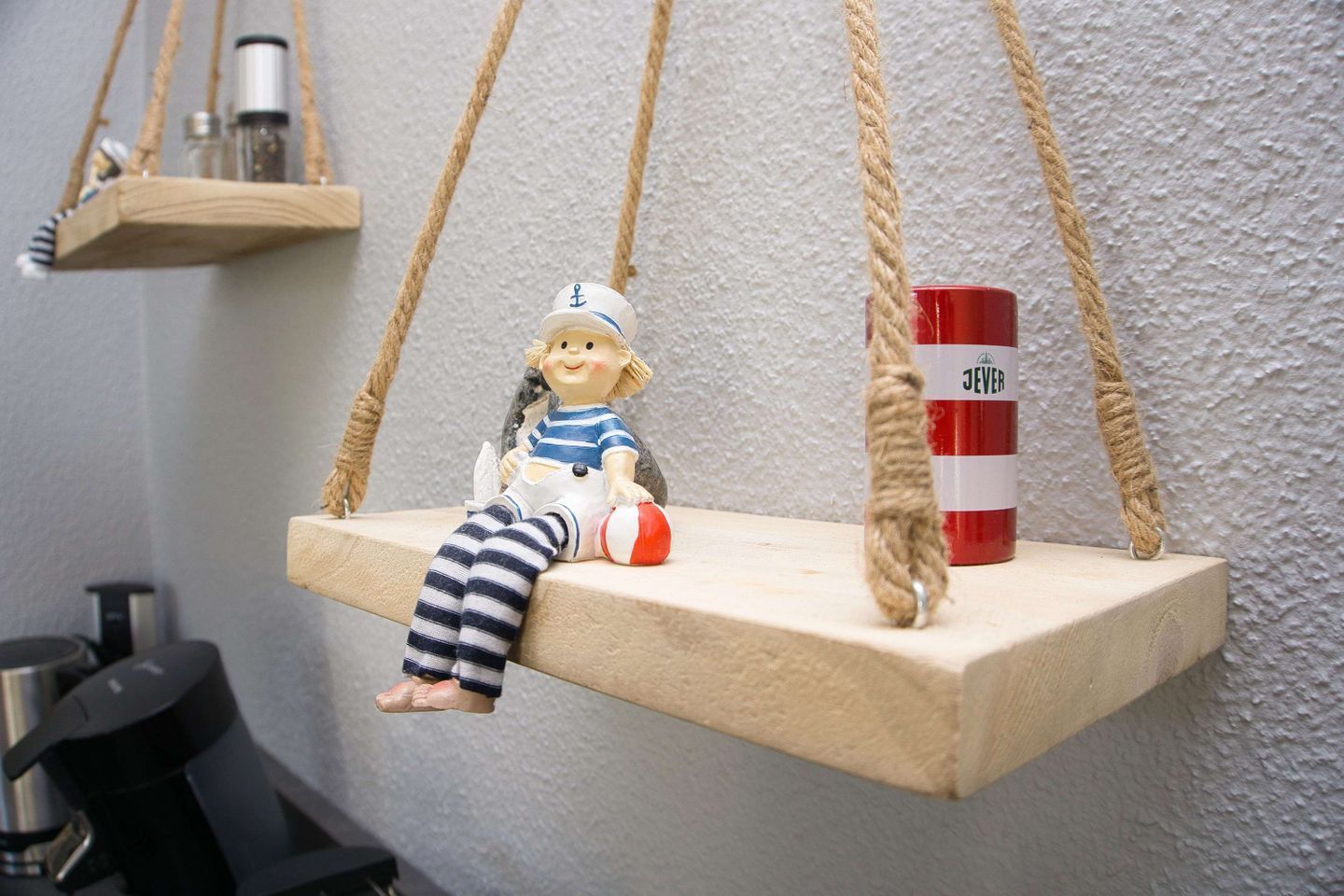 A doll sitting on a wooden swing suspended by ropes.