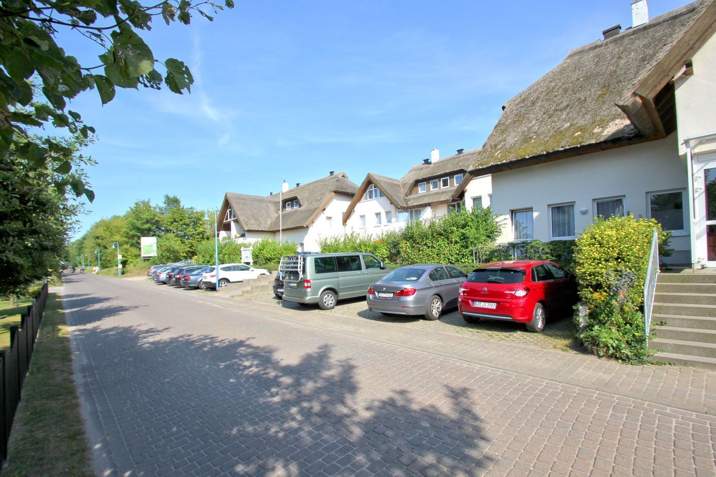 Une rue bordée de voitures garées et de maisons aux toits de chaume.