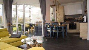 A modern living room with a yellow sofa, a glass coffee table, and a dining area with blue chairs.