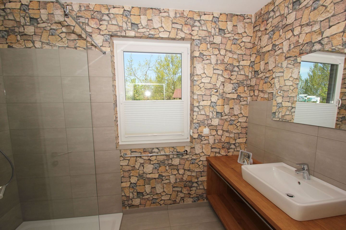 Un bagno con parete in pietra, una finestra, un lavandino e un box doccia.