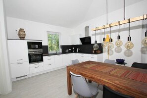 A modern kitchen with white cabinets, a black countertop, and a wooden dining table with chairs.
