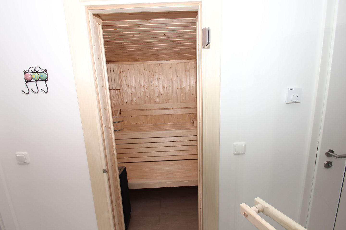 Una sauna de madera con un banco, un perchero y un panel de control en la pared.
