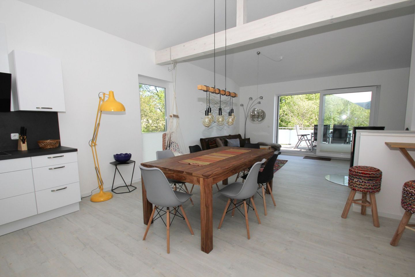 A modern kitchen with white cabinets, a wooden dining table, and a yellow floor lamp.