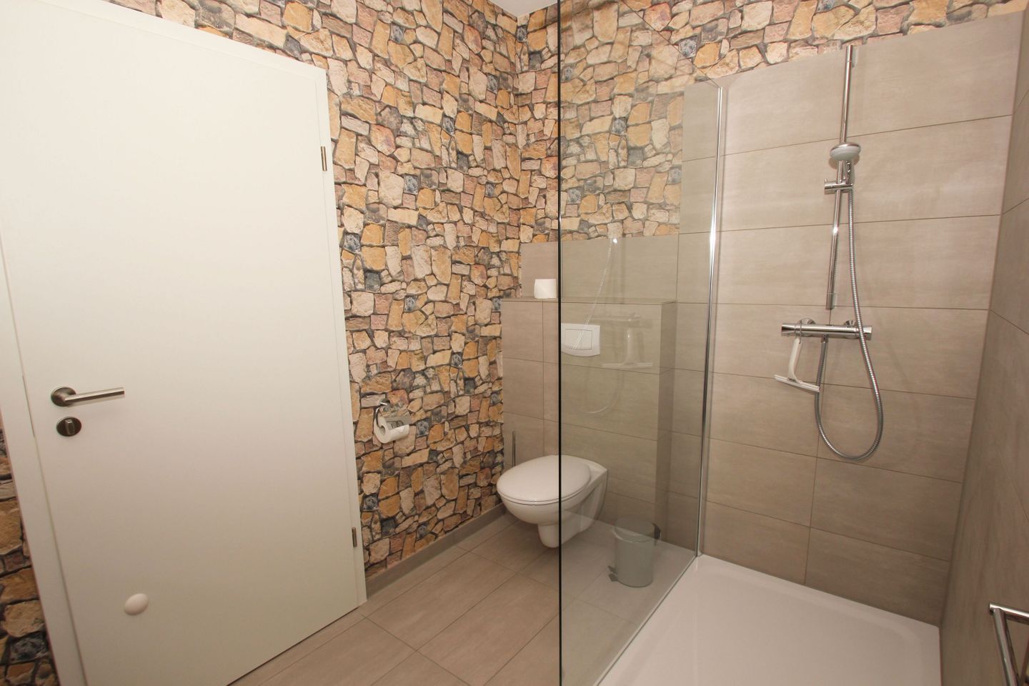 Un baño con ducha de vidrio, inodoro y pared de piedra.