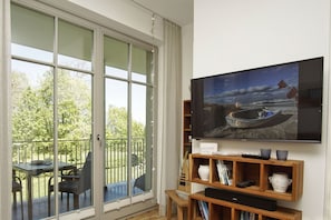 A living room with a TV, wooden shelves, and a balcony with a table and chairs.
