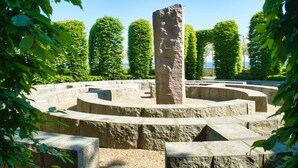 A stone monument surrounded by a circular stone pathway, with neatly trimmed hedges and trees in the background. - Modern vacation apartment with private sauna and balcony - Villa Pauline FeWo 04 - (Göhren)