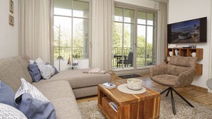 A living room with a sofa, armchair, coffee table, and a TV mounted on the wall. - Modern vacation apartment with private sauna and balcony - Villa Pauline FeWo 04 - (Göhren)