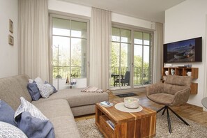 Ein Wohnzimmer mit Sofa, Sesseln, Couchtisch und einem an der Wand befestigten Fernseher.