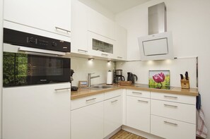 A modern kitchen with white cabinetry, a built-in oven, a coffee maker, and a sink.