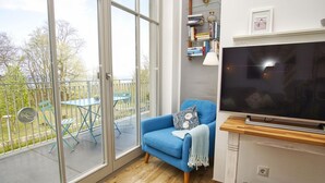 A room with a large window, a blue armchair, a flat-screen TV, and a bookshelf. - Modern vacation apartment with private sauna and balcony - Villa Pauline FeWo 07 - (Göhren)