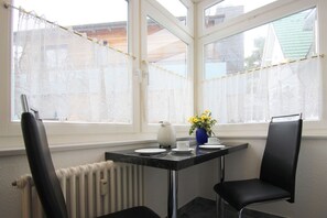 A small dining area with a table, two chairs, a vase with flowers, and a window with lace curtains. - Vacation apartment close to the beach in classic seaside style - Villa Stranddistel FeWo 2.7 (Binz)