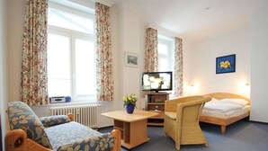 Ein gemütliches Zimmer mit Bett, einer Couch, einem Sessel, einem Fernseher und einer Heizung.