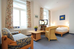 A cozy room with a bed, a sofa, a chair, a TV, and a radiator. - Vacation apartment close to the beach in classic seaside style - Villa Stranddistel FeWo 2.7 (Binz)
