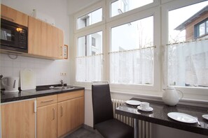 Una cocina moderna con armarios de madera, un microondas negro y una ventana con cortinas de encaje.