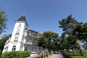 A white building with a tower, balconies, and a pathway lined with trees. - Vacation apartment close to the beach in classic seaside style - Villa Stranddistel FeWo 2.7 (Binz)