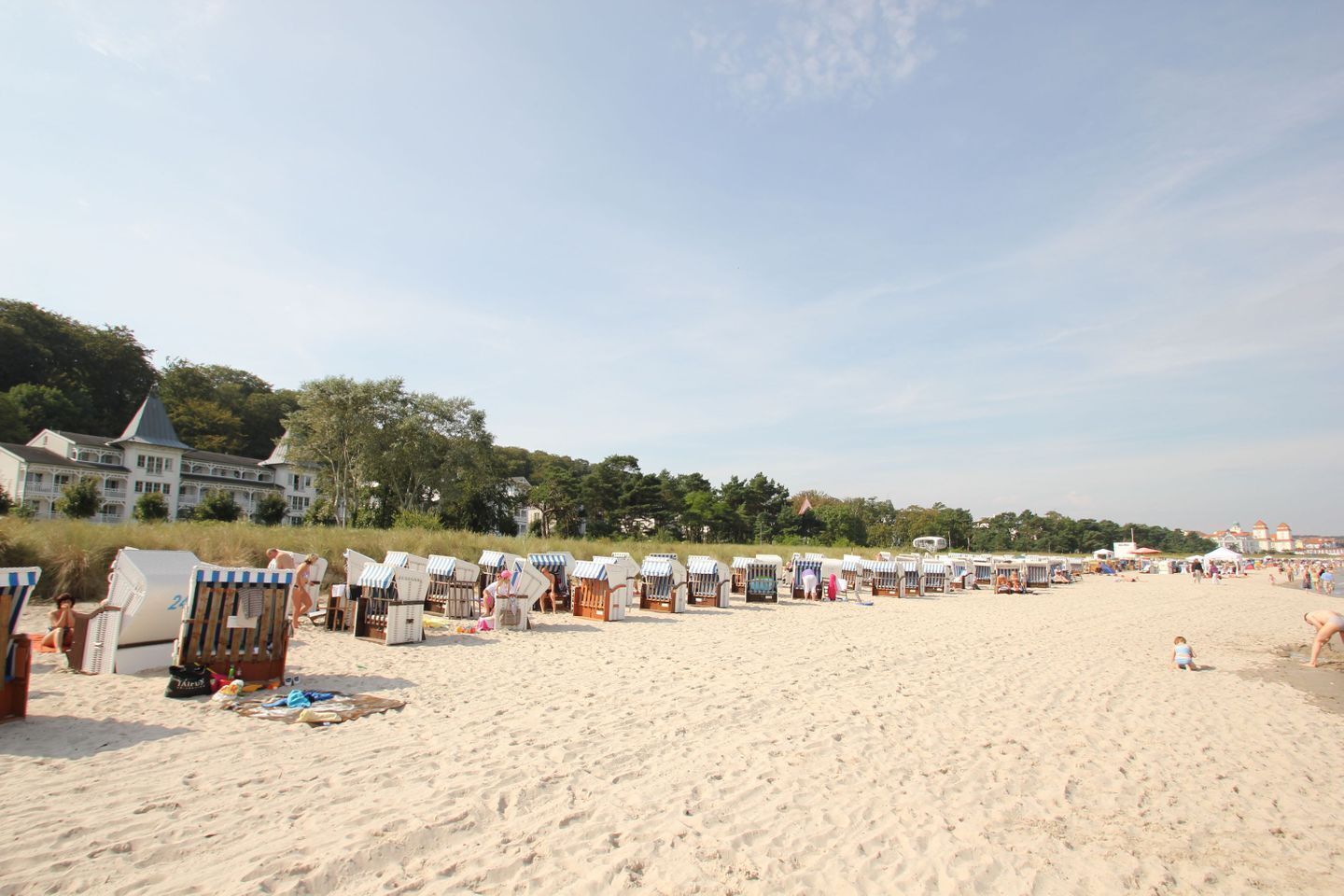Ein Strand mit Reihen aus Liegestühlen und Sonnenschirmen, ein großes Gebäude im Hintergrund und ein klarer Himmel.