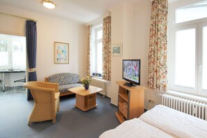 Una habitación de hotel con cama, televisor, sofá, sillón, una mesita y un radiador.