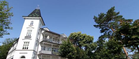 Un bâtiment blanc doté d’une tour, de balcons et d’un chemin bordé d’arbres.