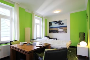 A hotel room with a bed, a desk, a chair, a bedside table, a lamp, and a window with curtains. - Beachfront vacation apartment in a classic seaside style - Villa Stranddistel FeWo 3.6 (Binz)