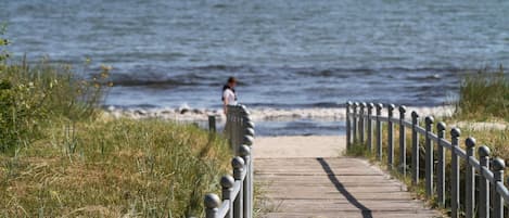 A wooden boardwalk leading to a beach with a person in the distance.
