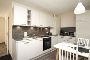 A modern kitchen with white cabinets, a black stove, a sink, and a dining area with a white table and chairs. - Inselhus Vacation Home - a small vacation home with a garden and terrace - Vacation Home (Glowe)