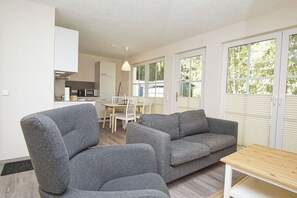 Una sala moderna con dos sofás grises, una mesa de centro de madera, y un comedor con una mesa y sillas blancas.