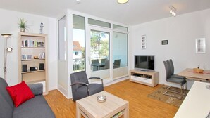 A modern living room with a grey sofa, a wooden coffee table, a TV, and a bookshelf. - Dünenresort Binz - beachfront, chic vacation apartment with balcony directly in Binz - (Binz)