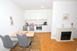 A modern kitchen with white cabinets, a dining table with chairs, and a fireplace.