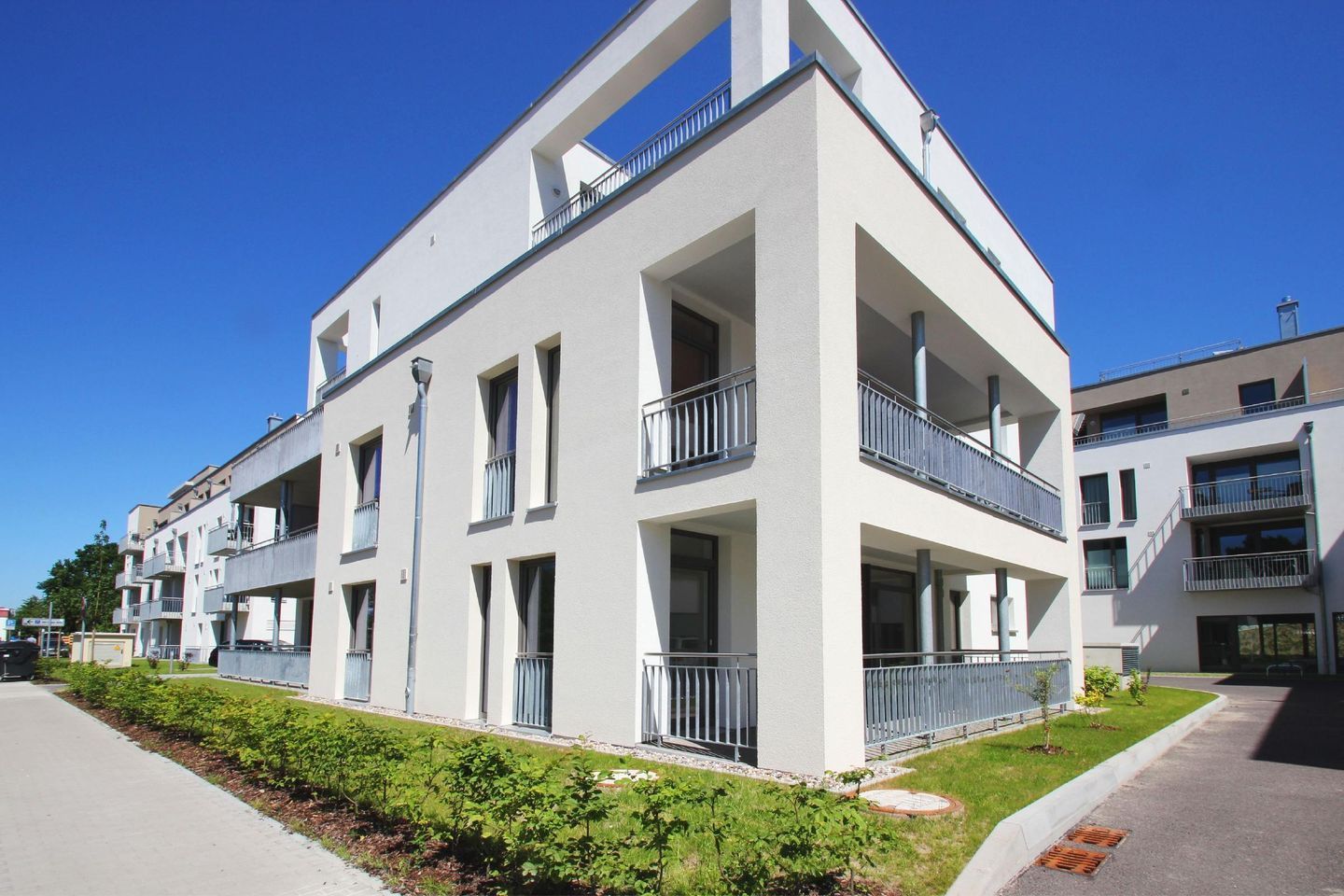 A modern multi-story residential building with balconies, a flat roof, and a clean, white exterior.