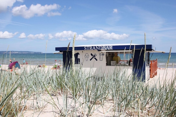 Rannalla sijaitseva ruokakioski nimeltä STRANDBAR, josta on esteetön näkymä merelle ja rannalle.