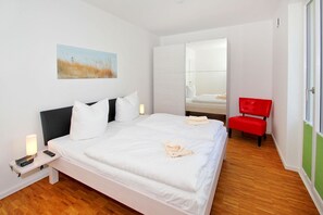 Une chambre d’hôtel moderne avec un grand lit, une table de chevet avec une lampe, un fauteuil rouge et un tableau au mur.