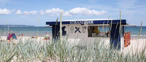 A beachside food kiosk named STRANDBAR with a clear view of the sea and beach in the background.