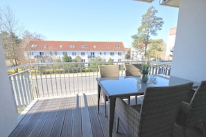 A balcony with a wooden deck, wicker chairs, a glass table, and a potted plant.