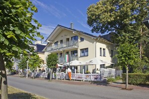 Un bâtiment à deux étages doté d’un balcon, d’un espace extérieur aménagé avec des parasols et d’une enseigne indiquant « Villa Wanzl ».