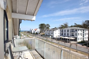 Ein Balkon mit Glasgeländer mit Blick auf eine Straße mit Gebäuden und blauem Himmel.