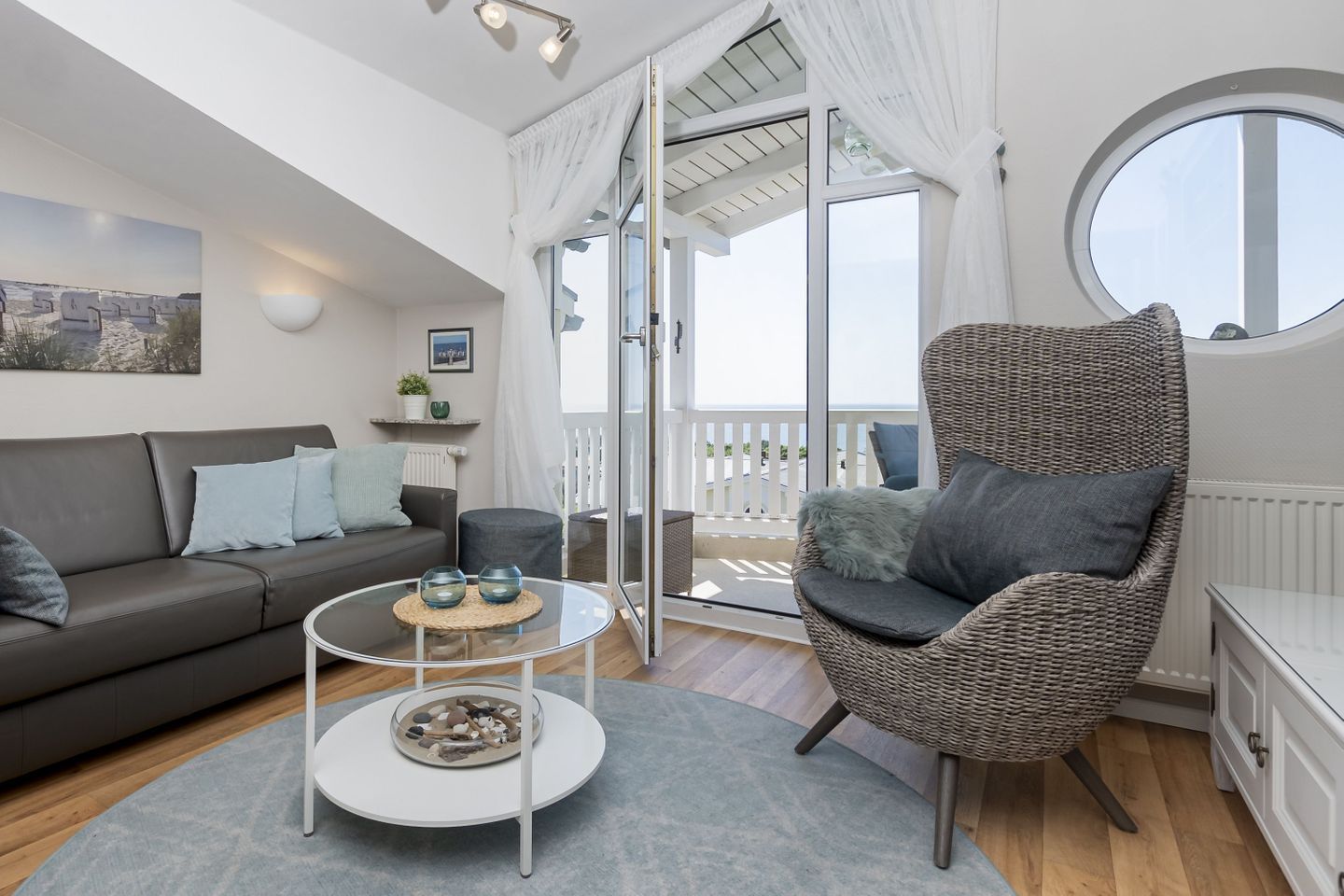 Un salon moderne avec un canapé gris, un fauteuil en osier et une table basse en verre.