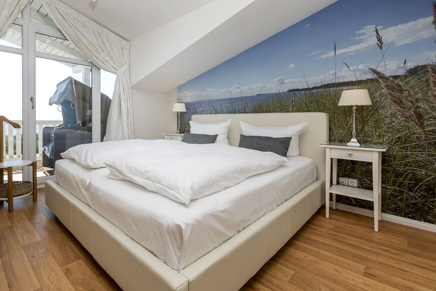 Une chambre avec un grand lit, une table de chevet avec une lampe, une chaise et une vue sur l’extérieur grâce à une porte vitrée.