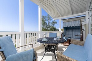 A covered outdoor seating area with wicker furniture and a table, overlooking a scenic view. - With a view of the sea and a balcony; access to the pool and sauna - Sea View Apartment 28 - (Göhren)