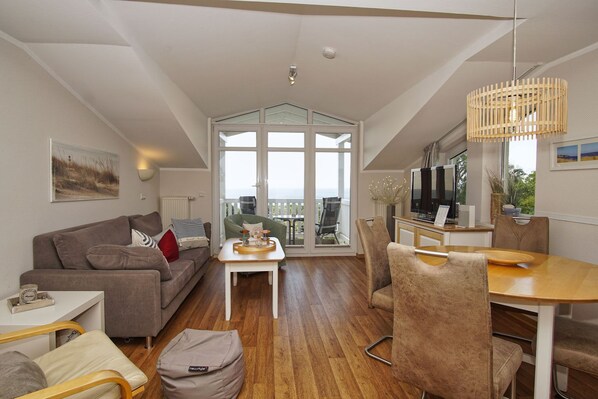 A spacious living area with a sofa, coffee table, and dining table. There is a balcony with a view.